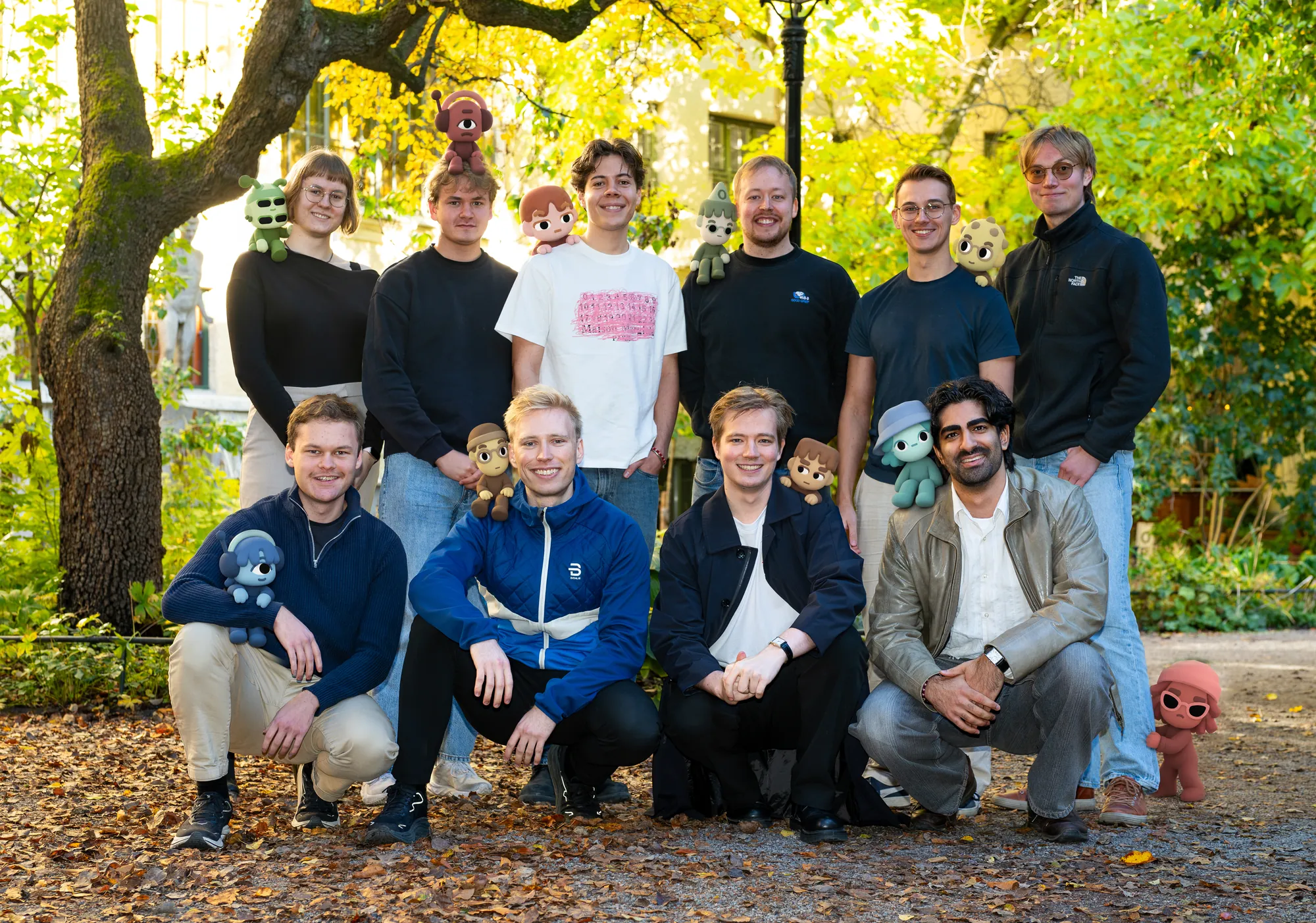 The Strawberry team, ten people outdoors under autumn trees, each with their own companion on a shoulder, head or lap.